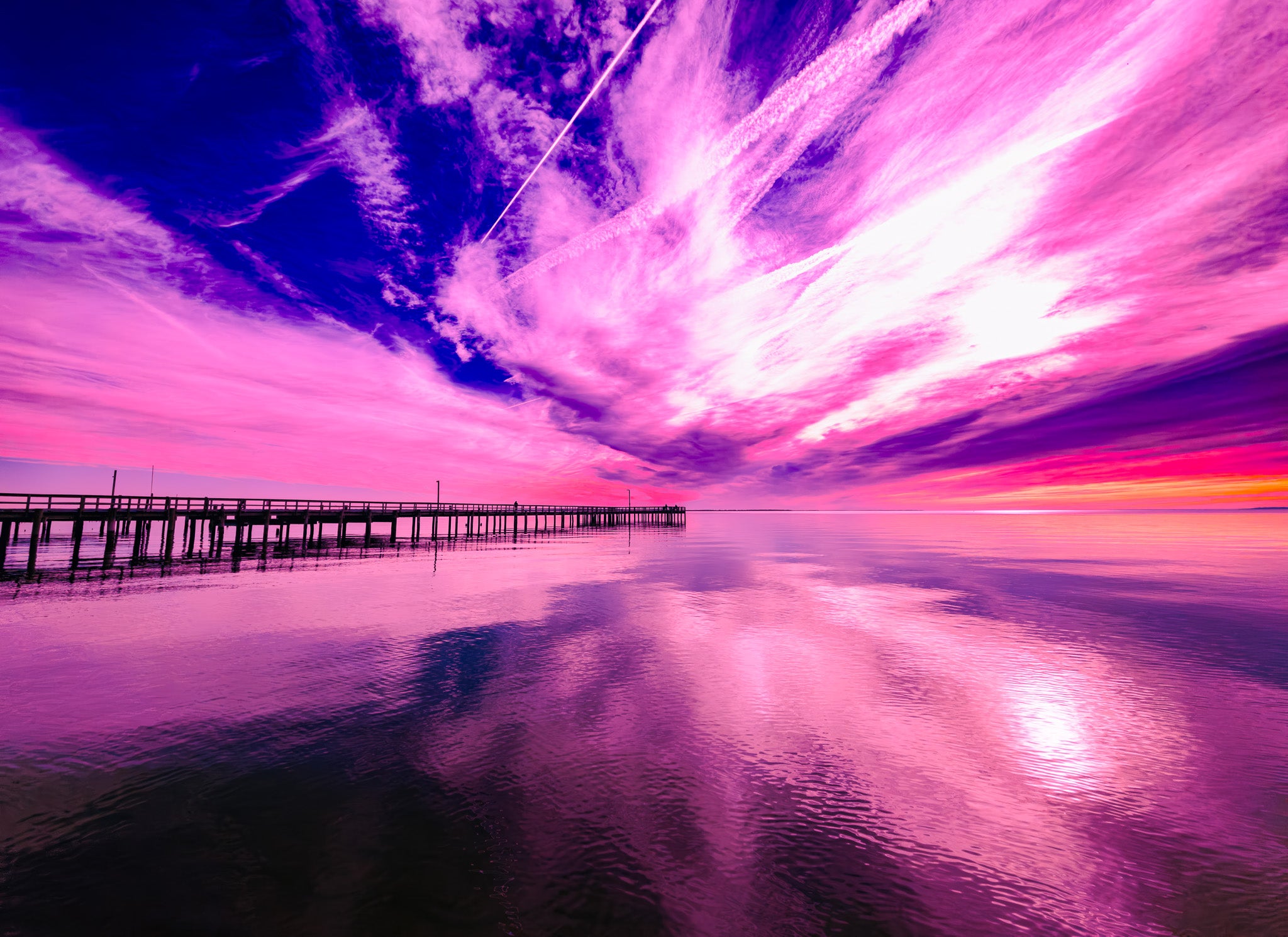 Vivid fine art photo of a pier over calm water at sunrise with dramatic pink and purple sky