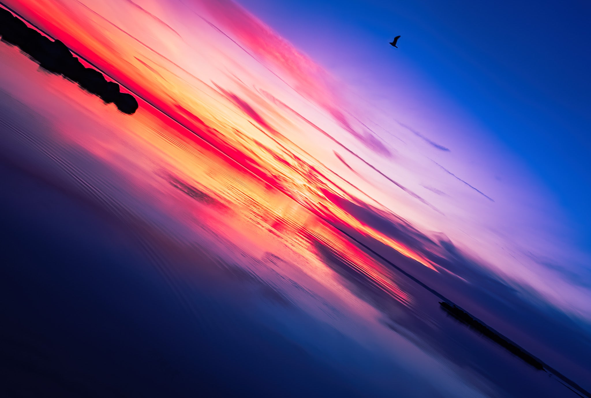 Angled view of orange and purple light over rippled water with a low sun near the horizon and layered clouds.