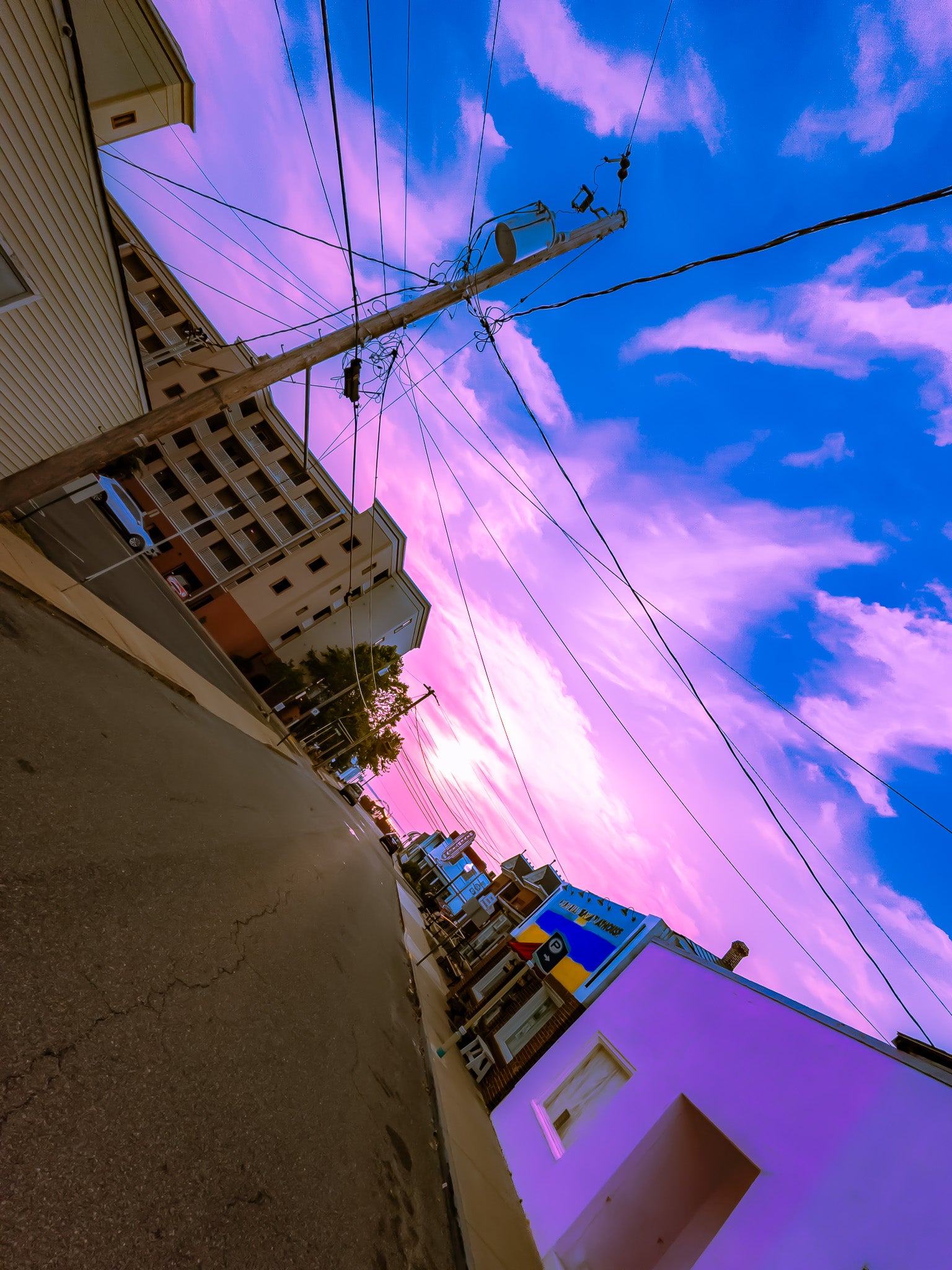 Angled street view at sunrise with a blue and pink sky, power lines, buildings, and a utility pole.