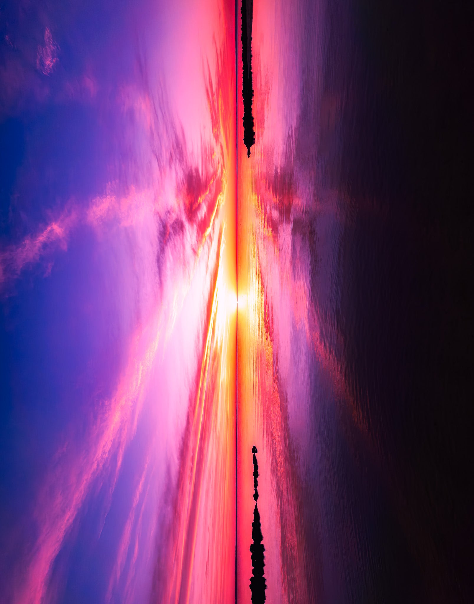 Angled view of a pink, purple, and orange sunset over water with rock barriers, cloud reflections