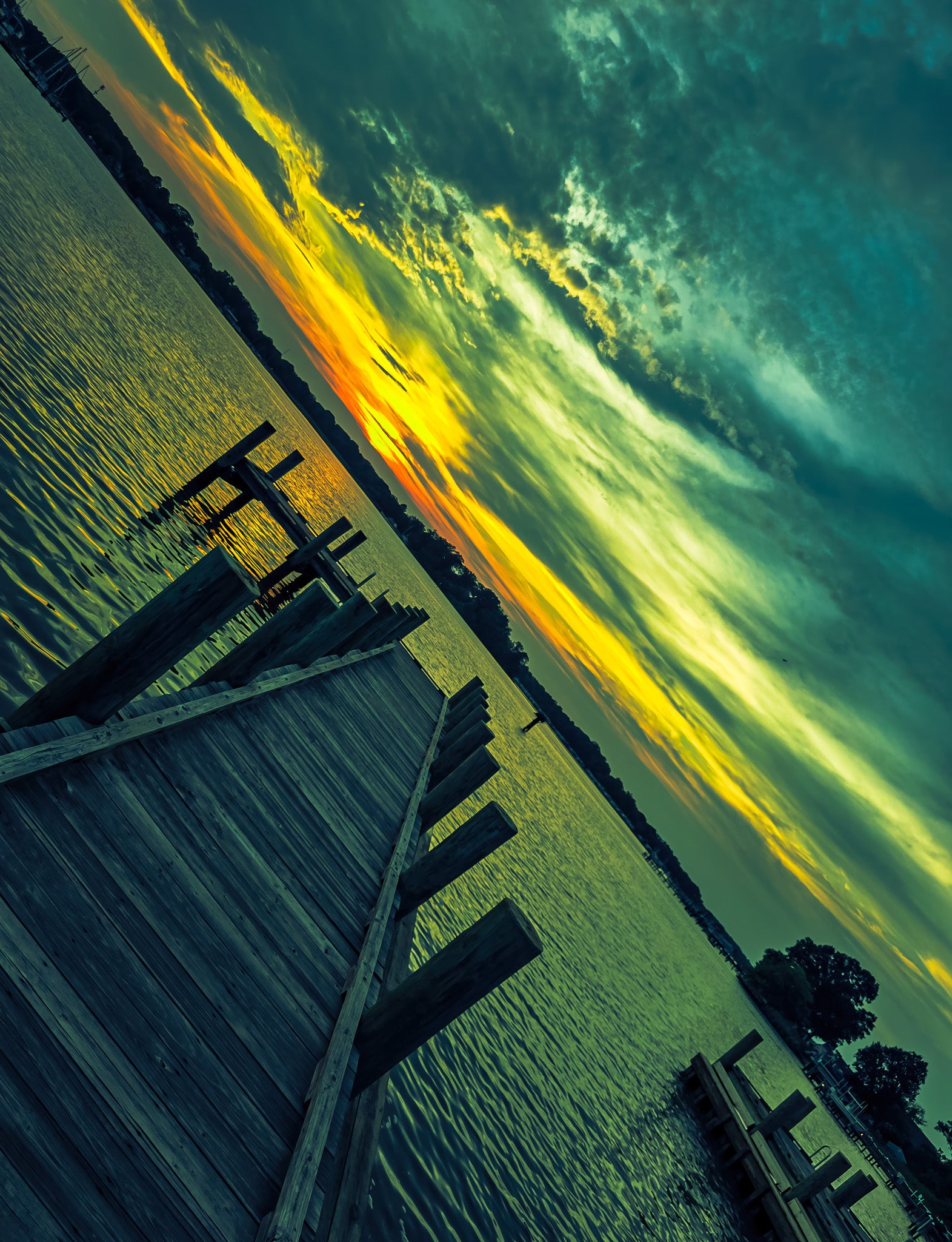 Angled view of a wooden dock at sunset with green and yellow clouds over rippled water.