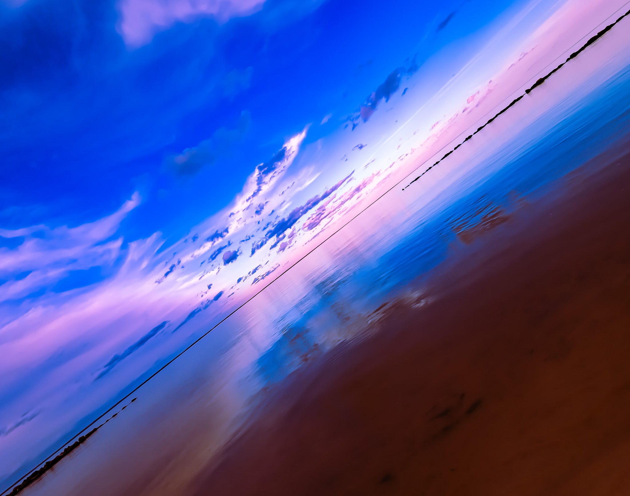 Angled view of a blue and pink sky over still water with soft reflections, a low horizon, and rock barriers at the edges.