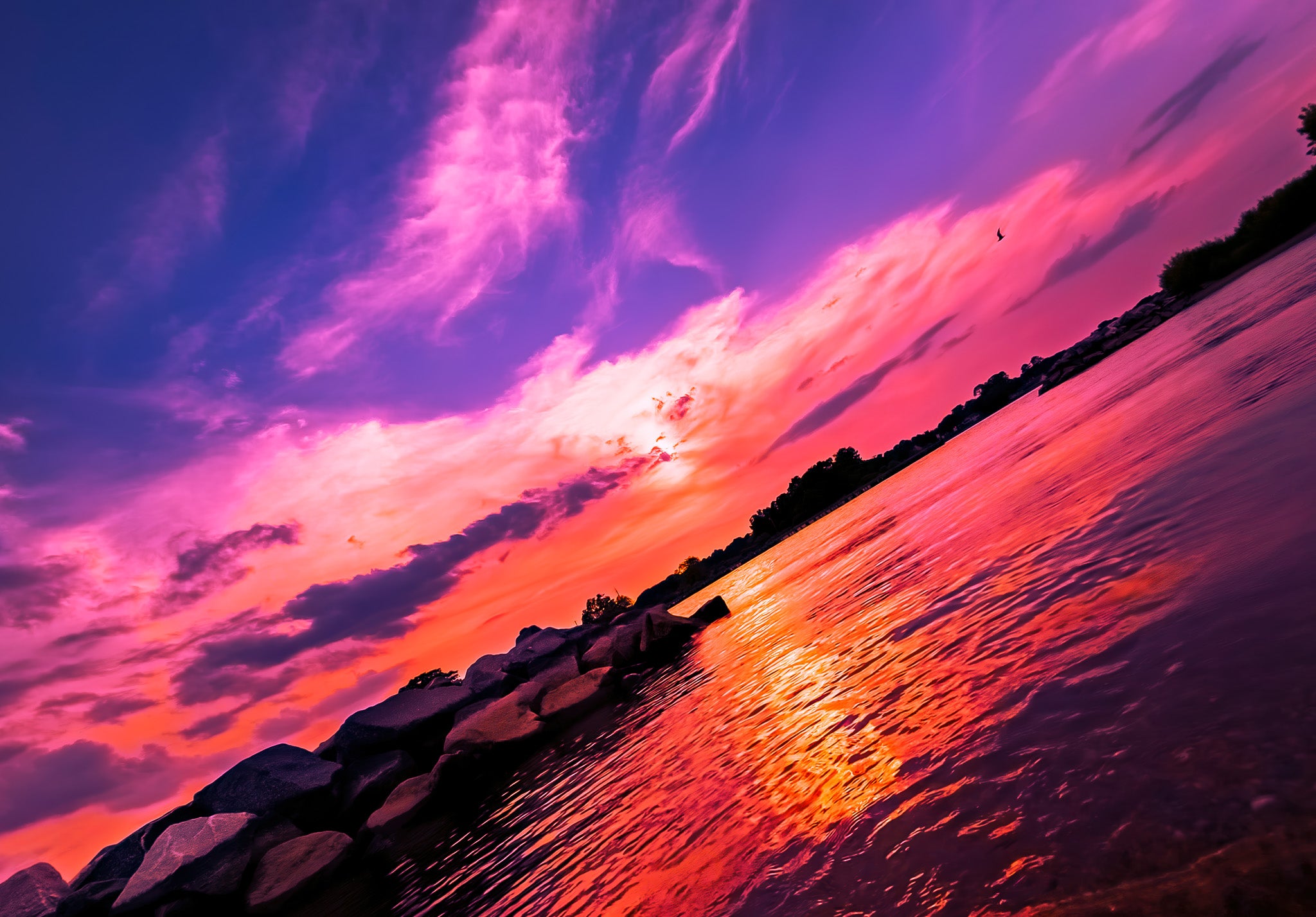 Sunset over water with vibrant purple and pink clouds reflecting on the water surface.