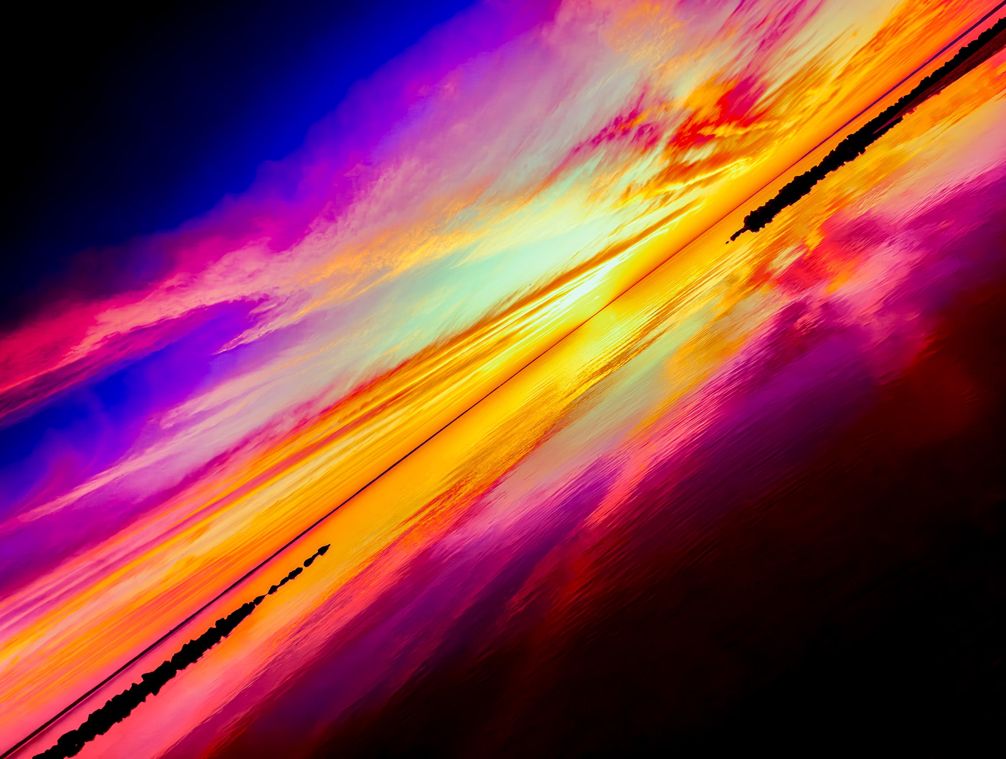 Angled view of a pink, purple, and orange sunset over water with rock barriers, cloud reflections