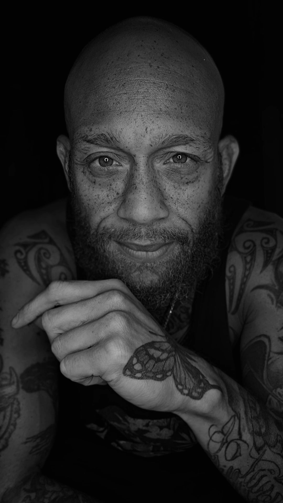 Black and white close-up portrait of a tattooed man with a beard, looking into the camera